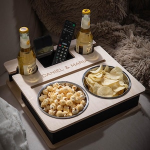 Könnte beinhalten: Ein Holz-Snacktablett mit zwei Schalen, eine gefüllt mit Popcorn und die andere mit Kartoffelchips. Es befinden sich zwei Flaschen Bier, eine Fernbedienung und ein Handy auf dem Tablett. Das Tablett ist mit den Namen "Daniel & Maria" personalisiert.