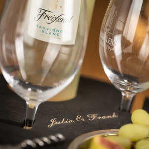 May include: A black slate serving tray with the words "Julia & Frank" engraved on it. A bottle of Freixenet Sauvignon Blanc wine is on the tray, along with two wine glasses, a corkscrew, and a bowl of fruit.