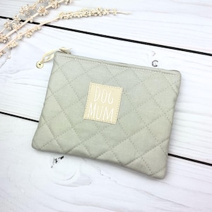 Può includere: Un astuccio trapuntato verde chiaro con chiusura a cerniera. L'astuccio presenta una toppa rettangolare con le parole "DOG MUM" in bianco. L'astuccio è realizzato in tessuto morbido e presenta un motivo a rombi.