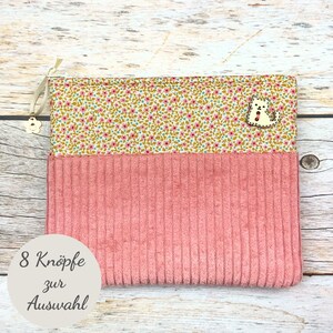 Könnte beinhalten: Eine rechteckige Reißverschlusstasche mit einem oberen Abschnitt aus gelbem Stoff mit kleinem rosa-blauem Blumenmuster und einem unteren Abschnitt aus rosa Cord. Ein weißer, katzenförmiger Holzknopf und ein blumenförmiger Reißverschlussanhänger.