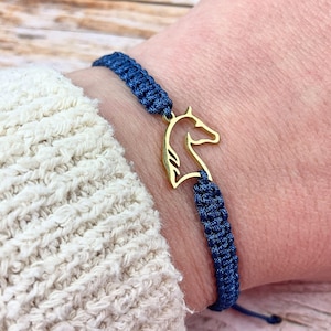 Könnte beinhalten: Ein marineblaues geflochtenes Armband mit einem goldfarbenen Pferdekopfanhänger. Das Armband ist geknotet und verstellbar. Der Anhänger ist eine stilisierte Umrisszeichnung eines Pferdekopfes.