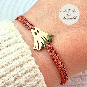 Könnte beinhalten: Ein Armband mit einem goldfarbenen Geister-Anhänger an einem rostfarbenen geflochtenen Band. Der Anhänger hat zwei Augenausschnitte und eine ausgestellte Basis. Ein weißer runder Aufkleber enthält den Text: viele Farben zur Auswahl.