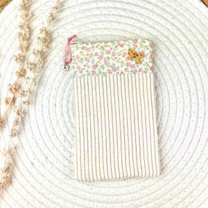 Könnte beinhalten: Ein rechteckiger Beutel mit einem floral gemusterten Oberteil und einem cordgestreiften Boden. Das Blumenmuster zeigt rosa und blaue Blumen auf weißem Hintergrund. Ein kleiner Lebkuchenmann-Knopf aus Holz ist angebracht.