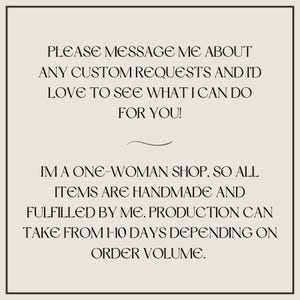 May include: A square sign with a light beige background and a thin black border. The text reads: PLEASE MESSAGE ME ABOUT ANY CUSTOM REQUESTS AND I'D LOVE TO SEE WHAT I CAN DO FOR YOU! I'M A ONE-WOMAN SHOP, SO ALL ITEMS ARE HANDMADE AND FULFILLED BY ME.