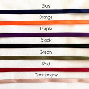 May include: A collection of six horizontal satin ribbons arranged in a stack. The colors from top to bottom are labeled as Blue, Orange, Purple, Black, Green, Red, and Champagne. Each ribbon is smooth, solid-colored, and uniform in width.