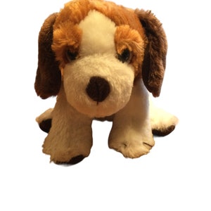 May include: A brown and white plush dog toy with brown ears and a white face. The dog is sitting with its paws tucked under its body.