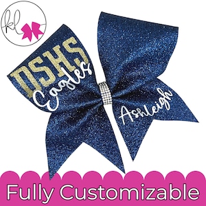 Op de afbeelding: Een donkerblauwe glitter haarstrik met de gouden glittertekst DSHS en de witte cursieve tekst Eagles aan de ene kant, en de naam Ashleigh in witte cursieve letters aan de andere kant. Het midden is versierd met een band van kleine strasssteentjes.