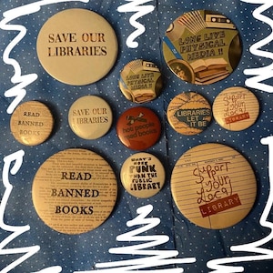 May include: A collection of vintage button pins with various designs and text. The pins feature phrases like "Save Our Libraries," "Read Banned Books," and "Support Your Local Library." The color palette includes beige, red, and green, with a blue polka dot background.