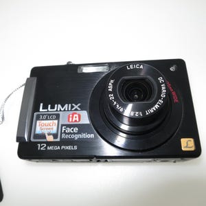 May include: A black Lumix digital camera with a Leica lens. The camera features a 3.0" LCD touch screen, face recognition, and 12 megapixels. The lens is labeled DC Vario-Elmarit 4.4-22 ASPH.