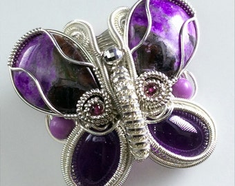 May include: A silver wire wrapped butterfly pendant with purple and green stones. The butterfly has a detailed design with small beads and wire accents.