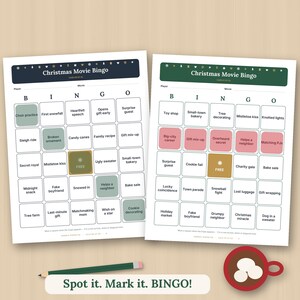 May include: Two Christmas Movie Bingo game cards with a grid of squares containing holiday-themed phrases. The left card has a dark blue header, and the right card has a green header. A green pencil and a red mug with marshmallows are nearby.