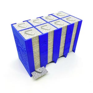 Puede incluir: Un soporte azul para cartas de juego con una pila de cartas. El soporte tiene un diseño decorativo en el lateral y contiene varias pilas de cartas. Las cartas tienen un patrón decorativo y la letra "C". La palabra "Carcassonne" está impresa en el lateral.