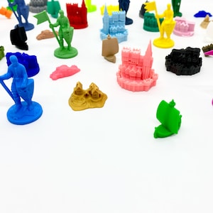 Può includere: Una collezione di miniature colorate per giochi, tra cui cavalieri, castelli e navi. I pezzi sono in vari colori come blu, verde, rosa e giallo. Alcune figure tengono bandiere. I pezzi sono sparsi su una superficie bianca.
