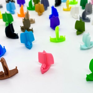 May include: A collection of colourful miniature wooden boats with sails. The boats are in various colours, including blue, green, red, yellow, and pink.