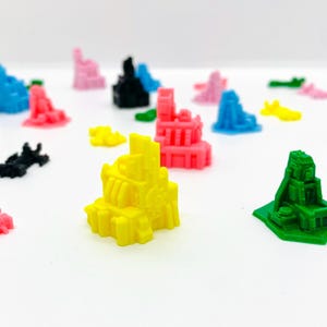 May include: A collection of colorful 3D printed miniature buildings in various styles and colors, including yellow, pink, blue, green, and black.
