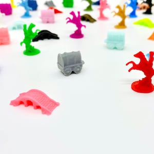 Könnte beinhalten: Eine Sammlung bunter Miniatur-Spielfiguren, darunter ein roter Ritter zu Pferd, eine rosafarbene Brücke, ein blauer Wagen und ein grauer Wagen. Die Figuren sind aus Kunststoff und für ein Brettspiel konzipiert.