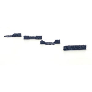 May include: Four miniature stone wall sections for tabletop gaming or model building. The walls are made of a dark gray material and are in various shapes and sizes.