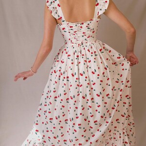 K&ouml;nnte beinhalten: Ein wei&szlig;es Kleid mit Kirschmuster. Das Kleid hat einen quadratischen Ausschnitt, R&uuml;schen&auml;rmel und einen R&uuml;cken im Korsett-Stil. Der Rock hat einen R&uuml;schensaum. Die Kirschen sind rot mit gr&uuml;nen Bl&auml;ttern.