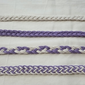 May include: Four braided cords in a row. The top cord is a light beige color. The second cord is a solid purple. The third cord is purple and white. The bottom cord is also purple and white.