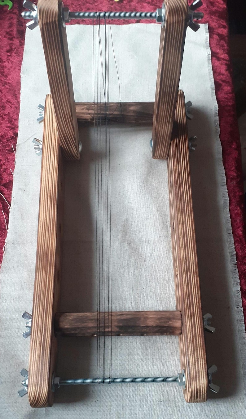 Puede incluir: Un telar de madera con hilo negro estirado a trav&eacute;s de &eacute;l. El telar est&aacute; hecho de madera marr&oacute;n oscura y tiene tornillos y tuercas de metal.
