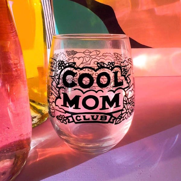 May include: A clear glass wine glass with a black design that says "Cool Mom Club".