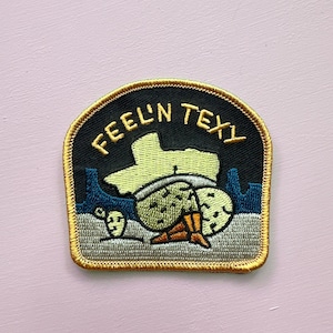 May include: Embroidered patch with a black background and gold trim. The patch features the words "FEEL'N TEXY" in gold lettering. The design includes a yellow outline of Texas, cacti, and a smiling face.