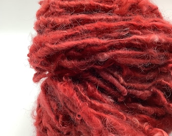 Op de afbeelding: Een bol rood garen met een pluche textuur. Het garen is losjes gewikkeld en heeft een paar witte vlekken.