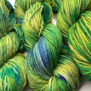Op de afbeelding: Een bol garen in groen, blauw en geel met een gevarieerd kleurpatroon. Het garen is zacht en pluizig en perfect om te breien of haken.
