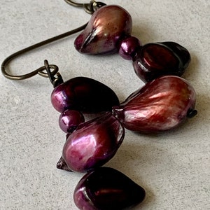 May include: A pair of earrings featuring a cluster of iridescent purple baroque pearls hanging from silver-toned hooks.
