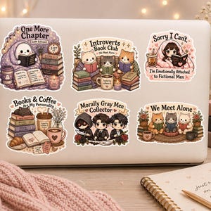 K&ouml;nnte beinhalten: Ein Laptop mit Aufklebern mit Buchmotiven. Die Aufkleber zeigen Illustrationen von lesenden Charakteren, B&uuml;cherstapeln und Kaffeetassen. Der Text enth&auml;lt "One More Chapter", "Introverts Book Club" und "Books & Coffee Are My Personality."