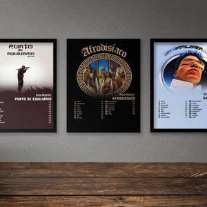 May include: Three framed album covers with black frames. The album covers are for the albums "Punto de Equilibrio", "Afrodisiaco", and "Saturno" by Rauw Alejandro. The album covers feature different artwork and text.