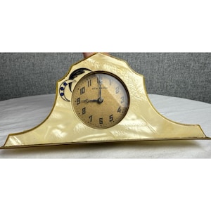 May include: An antique New Haven clock with a cream-colored, Art Deco-style case. The clock face is gold with black numerals and hands. A crescent moon and star design is on the upper left. The clock is approximately 8 inches wide.