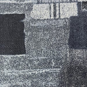 May include: Close-up of a fabric with a patchwork design. The fabric features a mix of dark and light blue denim-like textures, creating a textured, abstract pattern. The design includes rectangular and square shapes, with a dark blue border at the bottom.