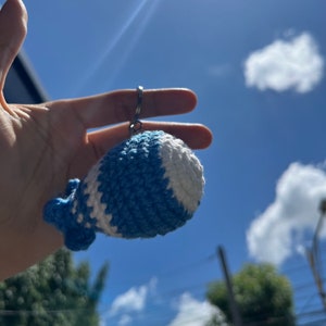 May include: A blue and white crocheted whale keychain hanging from a silver key ring.