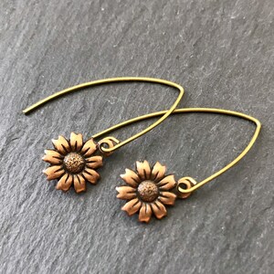 May include: A pair of gold-toned earrings with a copper-colored sunflower design. The earrings are made of wire and have a simple, delicate design.