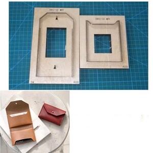 Puede incluir: Dos troqueles de corte de cuero de madera con recortes rectangulares, etiquetados "0811-10". Debajo, un tarjetero de cuero marrón y una cartera de cuero rojo sobre una superficie blanca.