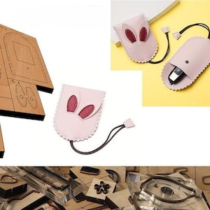 May include: A set of leather craft dies for making a small pink bunny-shaped pouch with a drawstring closure. The dies are made of metal and are arranged on a wooden surface. The pouch is shown in the image, with red bunny ears and a brown drawstring.
