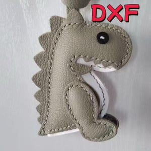 May include: A gray leather dinosaur keychain with a stitched outline and a black eye. The keychain has a loop at the top and the text "PDF", "DWG", and "DXF" in red.