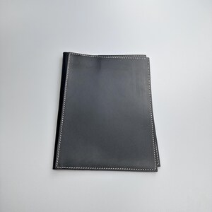 May include: A black leather portfolio with white stitching around the edges. The portfolio is rectangular and appears to be closed, with a smooth, matte finish. The stitching is a fine detail.