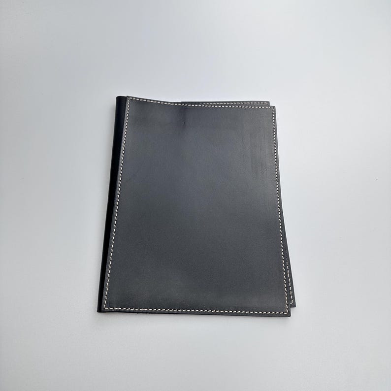 May include: A black leather portfolio with white stitching around the edges. The portfolio is rectangular and appears to be closed, with a smooth, matte finish. The stitching is a fine detail.