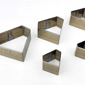 Puede incluir: Cinco cortadores de galletas en forma de diamante hechos de metal con un acabado de madera. Los cortadores son de diferentes tamaños y tienen medidas impresas. El cortador más grande tiene la palabra "KNIFE" impresa.