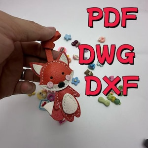 May include: A red and white fox-shaped leather keychain with a bow-shaped strap. The fox has white accents, pink cheeks, and a black nose. The image also includes the text "PDF", "DWG", and "DXF" in red.