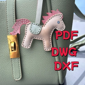 May include: A light pink leather horse charm with a pink mane and tail, a light blue saddle, and stitched details. The charm is attached to a green handbag. Text in red reads "PDF", "DWG", and "DXF".