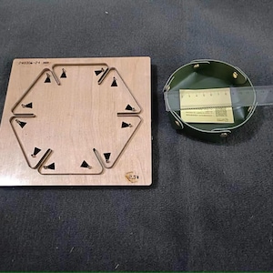May include: A wooden craft die with a hexagonal cutout and six triangular cutouts. The die is 2.5 inches in diameter. A green leather tray with brass rivets is next to the die.