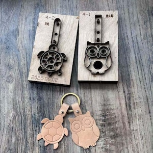 May include: Wooden craft tools for making leather keychains. The image shows a turtle and an owl design. The tools are made of wood and metal. The finished keychains are light brown and attached to a gold-coloured ring.