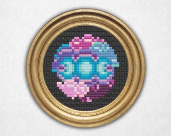 May include: A framed cross-stitch embroidery featuring a colorful, abstract design with pink, purple, blue, and green hues. The design is circular and resembles a flower or a mandala.