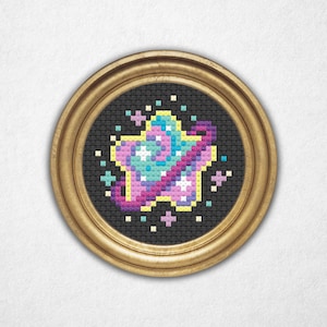 May include: A cross-stitch design of a star with a planet-like centre, framed in a gold-coloured, round frame. The star features shades of pink, blue, and yellow, with a purple swirl around it. The background is black.