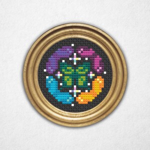 Könnte beinhalten: Ein gerahmtes Kreuzstich-Kunstwerk in runder Form. Das Design zeigt ein zentrales grün-weißes Motiv, umgeben von Segmenten in Blau, Orange, Lila und Rosa. Das Kunstwerk befindet sich auf schwarzem Hintergrund und in einem goldfarbenen, runden Rahmen.