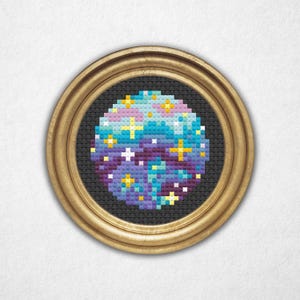 May include: A framed cross-stitch design of a galaxy with purple, blue, and pink colors and yellow stars.