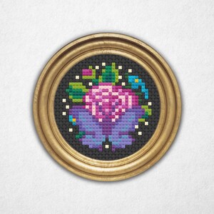 May include: A round, gold-framed cross-stitch picture. The artwork depicts a floral design in purple, pink, green, and blue on a black background. The piece is a decorative item, suitable for wall display. The frame is circular.